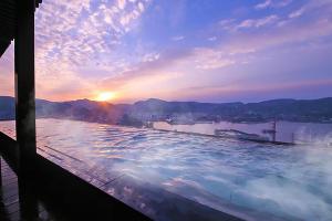 a large swimming pool with the sunset in the background at Ooedo Onsen Monogatari Nagasaki Hotel Seifu in Nagasaki