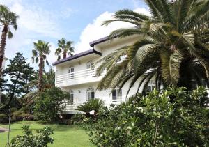 a white house with palm trees in front of it at Jeju Resortel in Jeju