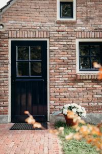 una casa de ladrillo con una puerta negra y dos ventanas en Relaxed eigen plekje in de Peel - Kostelijk, en Helenaveen