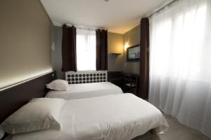 two beds in a hotel room with a window at Citadel Hôtel in Calais