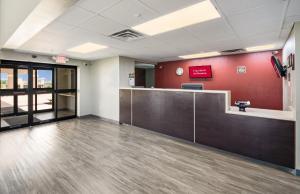 un vestíbulo de oficina con recepción y pared roja en Red Roof Inn & Suites Austin East - Manor, en Manor