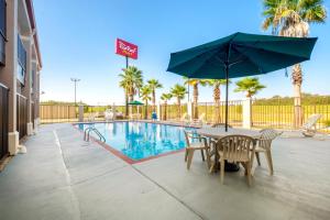 a table with chairs and an umbrella next to a pool at Red Roof Inn PLUS+ Hammond in Hammond