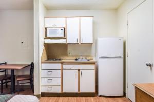 a kitchen with a white refrigerator and a table at HomeTowne Studios by Red Roof Dallas - North Addison - Tollway in Addison