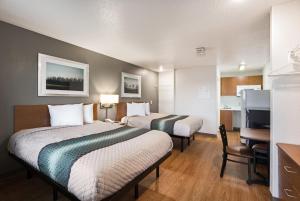 a hotel room with two beds and a desk at HomeTowne Studios by Red Roof Detroit - Livonia in Livonia
