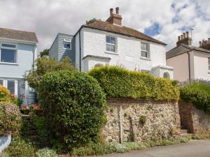 a white house behind a stone wall with bushes at Kits Cottage in Hythe