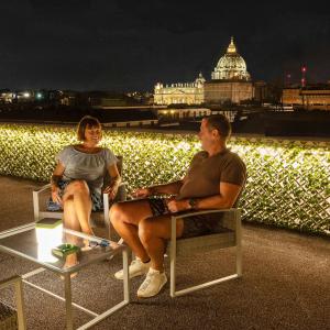 a man and woman sitting in chairs on a balcony at night at Hotel Relais Dei Papi in Rome