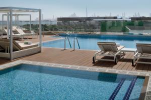 Holiday Inn & Suites - Dubai Festival City Mall, an IHG Hotel في دبي: مسبح مع كرسيين وفيسفور