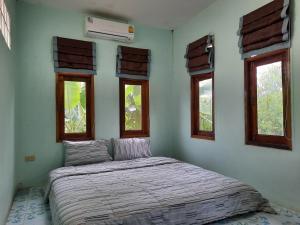 a bed in a room with three windows at Heuan Na Khee in Udon Thani