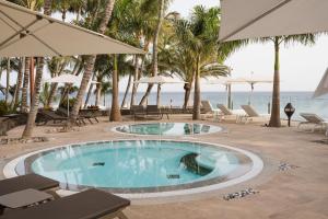 a swimming pool at the beach with chairs and umbrellas at Hotel Fariones in Puerto del Carmen
