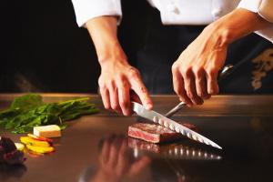 a person cutting meat with a knife on a counter at ANA InterContinental Manza Beach Resort by IHG in Onna