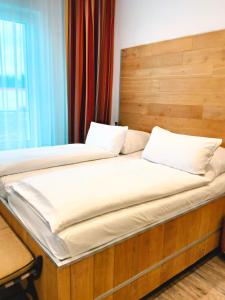 a bed with a wooden headboard and white pillows at DONAUHOTEL Ingolstadt in Ingolstadt