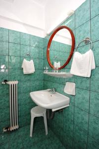 Baño de azulejos verdes con lavabo y espejo en Pergamos Hotel, en Atenas