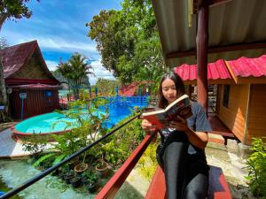 Una donna seduta su una ringhiera che legge un libro di Rapala Rock Wood Resort- SHA Plus a Railay Beach