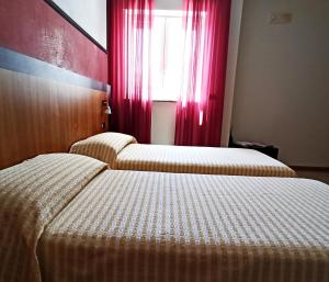 zwei Betten in einem Zimmer mit Fenster und roten Vorhängen in der Unterkunft Hotel Naitendì in Cutrofiano