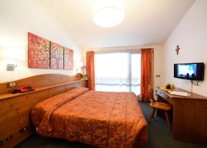 um quarto com uma cama, uma secretária e uma televisão em Hotel Corona em Val di Zoldo