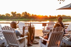 a group of people sitting in lawn chairs by a lake at Zambezi Mubala Campsite in Katima Mulilo