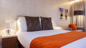 - une chambre avec un grand lit blanc et une couverture orange dans l'établissement Crowne Plaza London Kings Cross, an IHG Hotel, à Londres