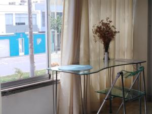 une table en verre avec un vase de fleurs sur elle à côté d'une fenêtre dans l'établissement Hospedaje de Lidia, à Lima