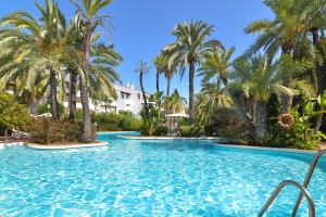 a swimming pool with palm trees in a resort at Luxurious beachside in the heart of Puente Romano in Marbella