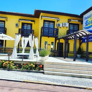 un edificio amarillo con sombrillas blancas delante en Pousada do Bosque, en Rio das Ostras