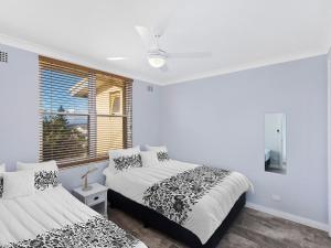 a white bedroom with two beds and a window at Golden Sands Apartment 10 in The Entrance