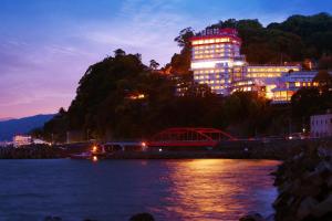 un edificio illuminato di notte accanto a un fiume di Ooedo Onsen Monogatari Hotel Suiyotei ad Atami