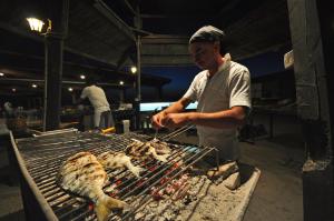a man is cooking chickens on a grill at Hotel Corsaro Nero in Portu Maga