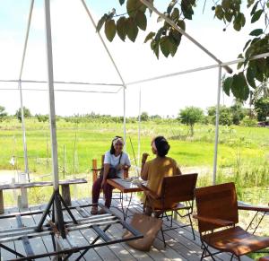 Due donne sedute a un tavolo sotto una tenda di Raina-Suanpa Lung Sood Farmstay a Suphanburi