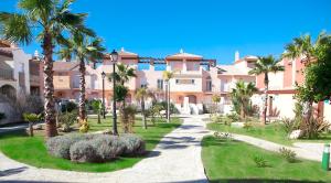 a large pink building with palm trees and a walkway at Zahara Sol Villas y Apartamentos by QHotels in Zahara de los Atunes