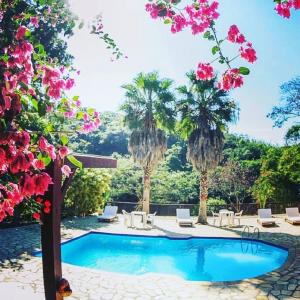 uma piscina com palmeiras e flores cor-de-rosa em Pousada Casa Cactus Praia da Tartaruga Búzios em Búzios