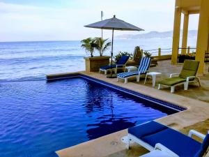 a swimming pool with chairs and an umbrella next to the ocean at Hotel Bogavante in Barra de Navidad