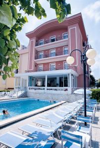 a large pink building with a swimming pool and lounge chairs at Hotel Clitunno in Misano Adriatico