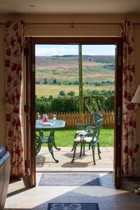 Otwarte drzwi na patio ze stołem i krzesłami w obiekcie Finest Retreats - Quail's Nest Cottage w mieście Edlingham