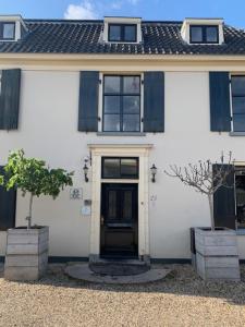 a white house with a black door and two trees at Bed & Breakfast Geesberge in Maarssen