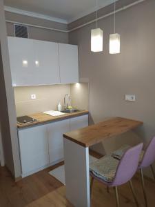 una cocina con armarios blancos y una mesa y sillas de madera. en Lia Apartman en Nyíregyháza