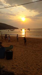 een groep mensen die bij zonsondergang op het strand spelen bij Nena's Suítes in Praia de Araçatiba