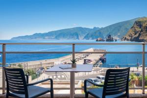 a table and chairs on a balcony overlooking the water at Aqua Natura Bay in Porto Moniz