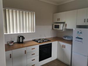 a kitchen with white cabinets and a stove and a microwave at Muir Holiday Apartments in Stilbaai