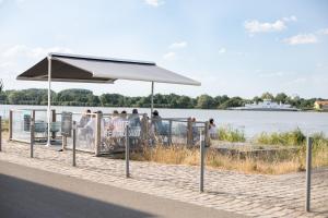 a pavilion on the side of the water with people sitting under it at L'Esplanade in Le Pellerin