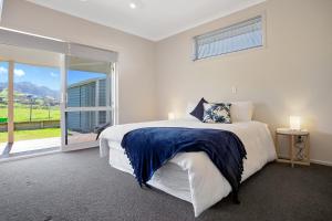 a white bedroom with a bed and a large window at Sky Blue Retreat - Waihi Beach Holiday Home in Waihi Beach