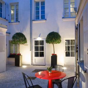 une table rouge et des chaises devant un bâtiment blanc dans l'établissement Hotel Saint Dominique, à Paris