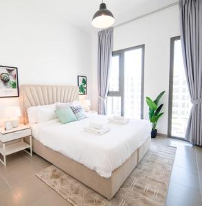 a white bedroom with a large bed and windows at GuestReady - Flutes of Harmony in Town Square in Dubai