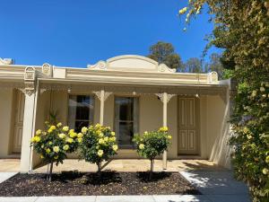 a white house with two trees and yellow flowers at Acacia Terraces in Echuca