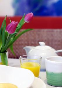 een tafel met een vaas met bloemen en een glas sinaasappelsap bij 1st Creatif Hotel Elephant in München
