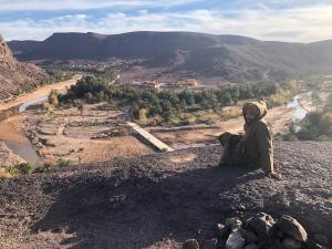 una persona sentada en la cima de una colina con vistas a un río en Maison d'hôtes Dar Farhana, en Ouarzazate