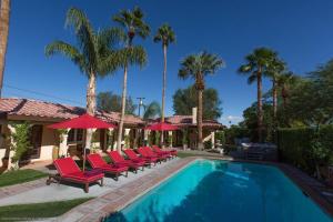 a swimming pool with red lounge chairs and palm trees at Villa Cristine - Spanish Style Palm Springs Villa in Palm Springs