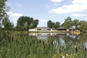 a lake with buildings in the background and grass at Duckling View in South Cerney