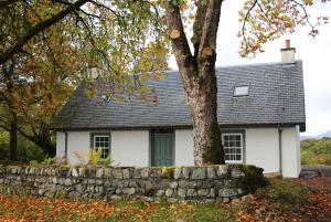 una casa blanca con un árbol y una pared de piedra en Pirn Mill Self Catering Cottage, en Cladich