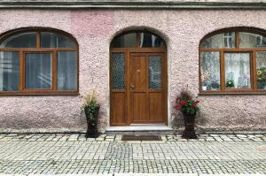 różowy budynek z drewnianymi drzwiami i dwoma oknami w obiekcie Za Rogiem w mieście Duszniki Zdrój