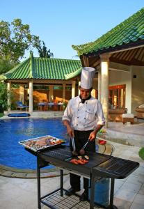 Um homem está a preparar comida numa grelha. em Bali Emerald Villas em Sanur